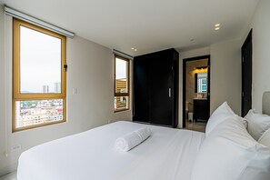 Ein Hotelzimmer mit einem großen Bett, einem Badezimmer mit Spiegel und Blick auf die Stadtlandschaft durch das Fenster.