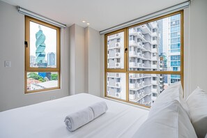 Ett hotellrum med en säng, ett fönster med utsikt över stadsbilden och utsikt över en bostadsbyggnad.