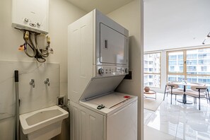 Ett kompakt kök med inbyggd tvättmaskin och torktumlare, ett handfat och ett fönster med utsikt över stadsbilden.