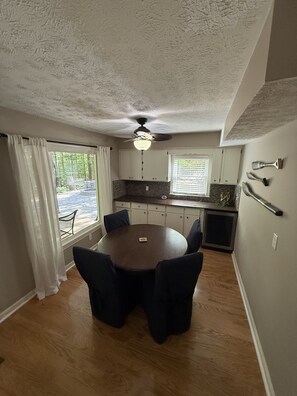 A dining area with a round table, chairs, a ceiling fan, and a view of a stone patio outside.