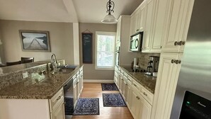 Una cocina con armarios blancos, encimeras de granito, un refrigerador de acero inoxidable y una ventana con persianas.