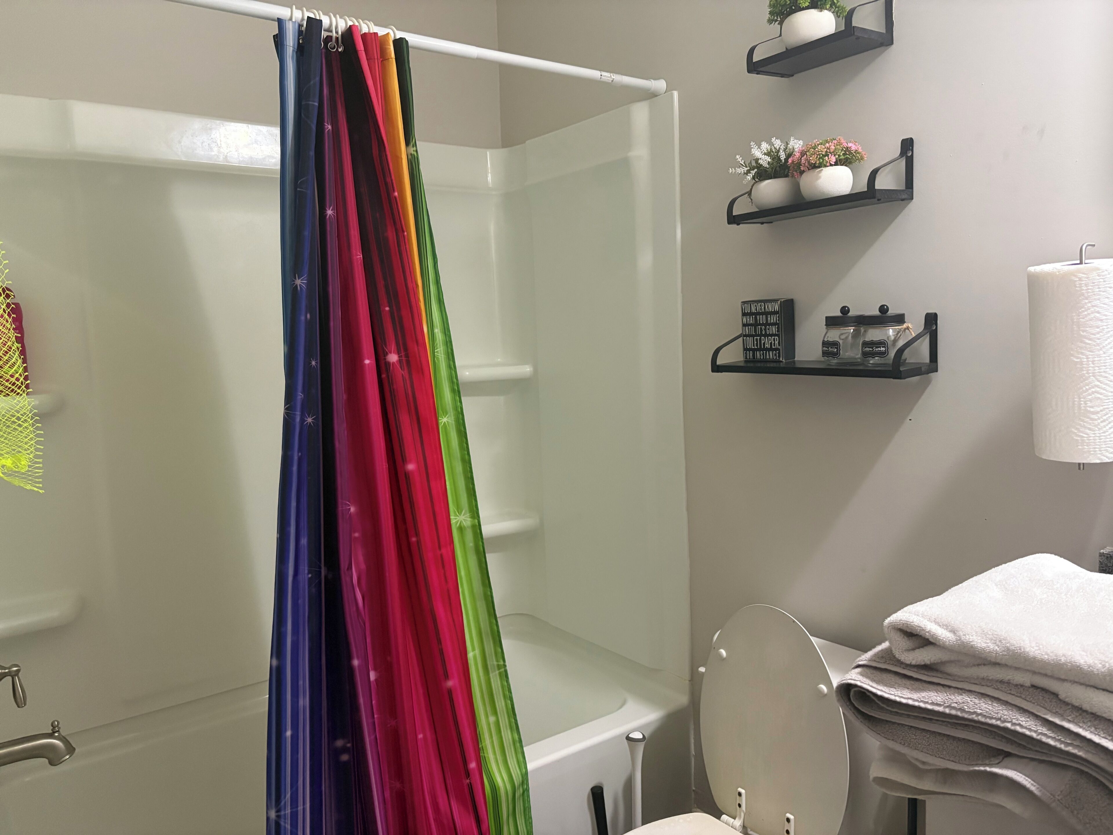 A bathroom with a shower curtain, toilet, sink, and shelves with toiletries.