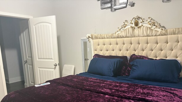 A bedroom with a tufted headboard, a bed with a purple velvet bedspread, two blue pillows, and a remote control on the bed. - Charming 3-bedroom house pleasant Dallas (dallas)