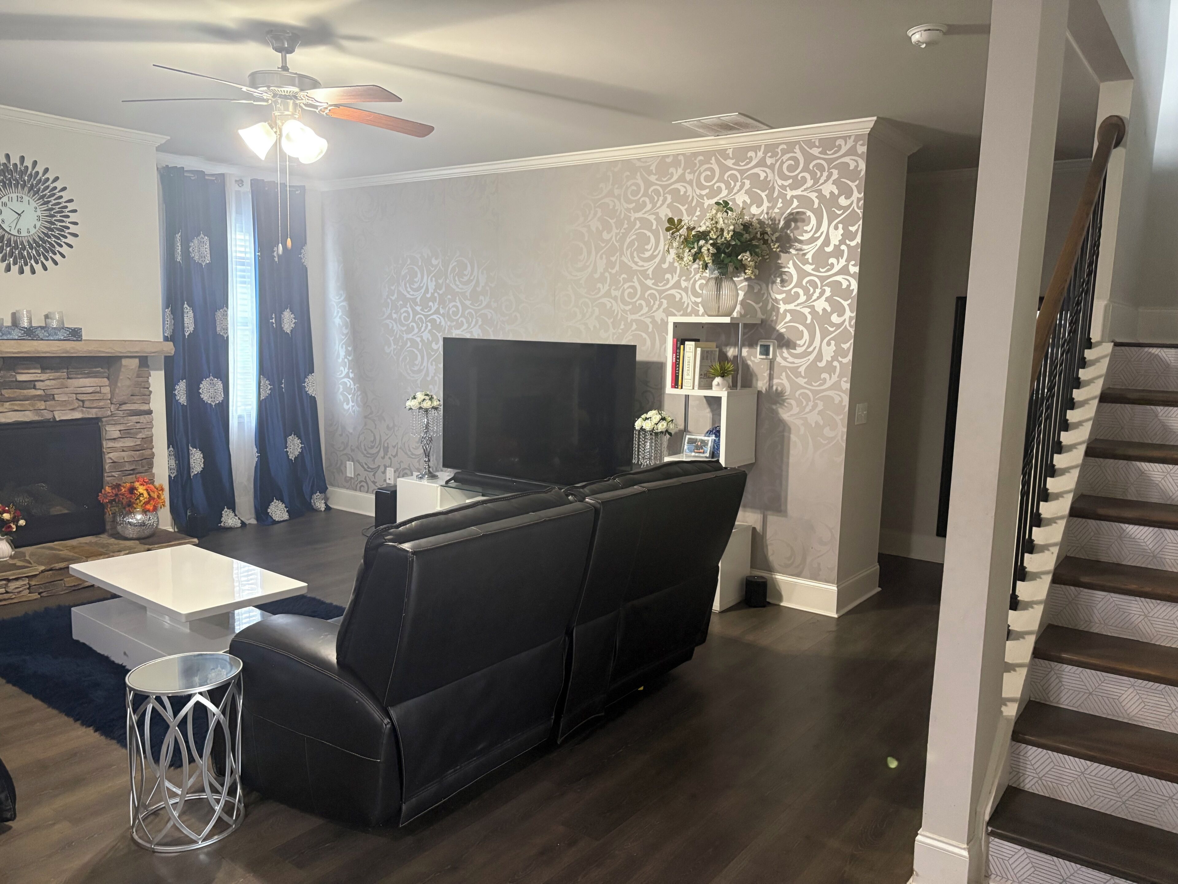 A living room with a black leather sofa, a flat-screen TV, a fireplace, and a staircase.