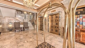 Eine prachtvolle Lobby mit Marmorböden, einem Kristalllüster, einer Treppe und einer Rezeption.