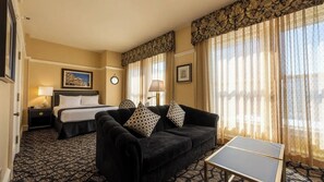 Ein Hotelzimmer mit einem Bett, einem Sofa, einem kleinen Tisch und einem fenster mit Vorhängen.