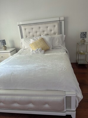 A neatly made bed with white bedding, a tufted headboard, and a bedside table with a lamp.