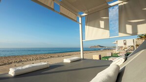 Un'area relax in spiaggia con vista sul mare, un lettino e un piccolo edificio sullo sfondo.