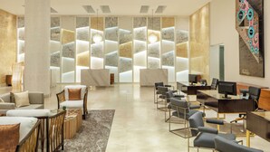 Un'area reception moderna con una scrivania in marmo, diverse opzioni di seduta tra cui divani e poltrone, e un grande dipinto astratto appeso alla parete.
