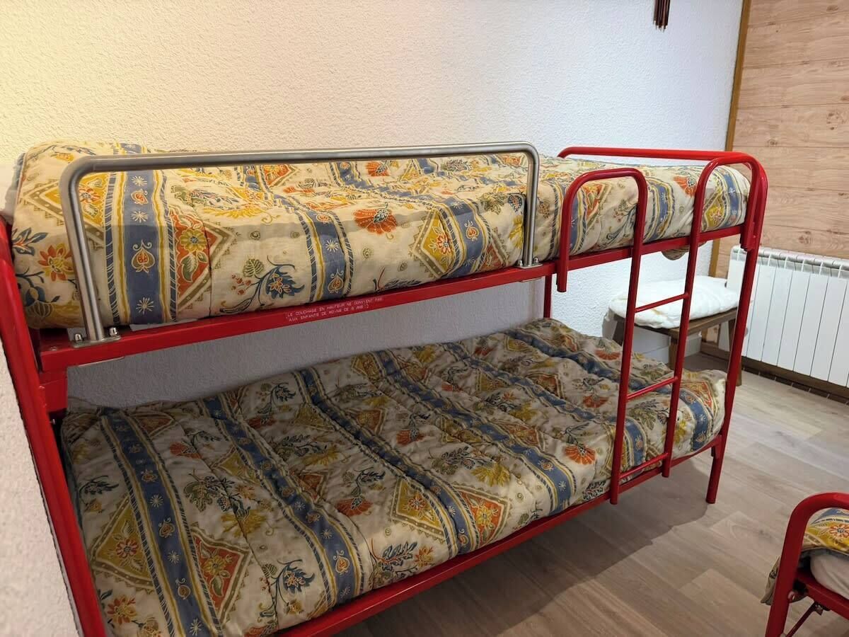 Una cama litera con ropa de cama estampada, estructura de metal rojo y suelo de madera.