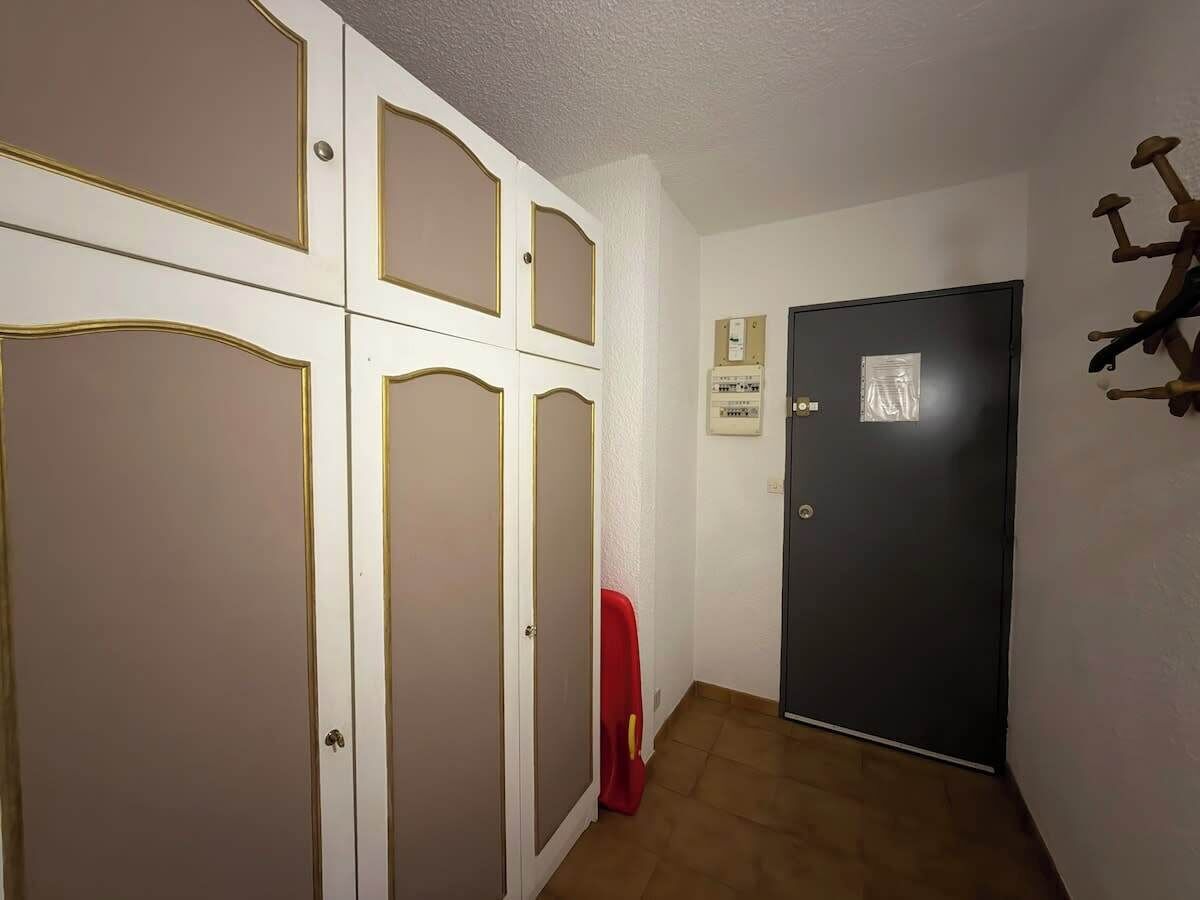 Un couloir avec une porte fermée, une chaise rouge et un luminaire fixé au mur.