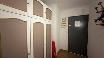 Un couloir avec une porte fermée, une chaise rouge et un luminaire fixé au mur.
