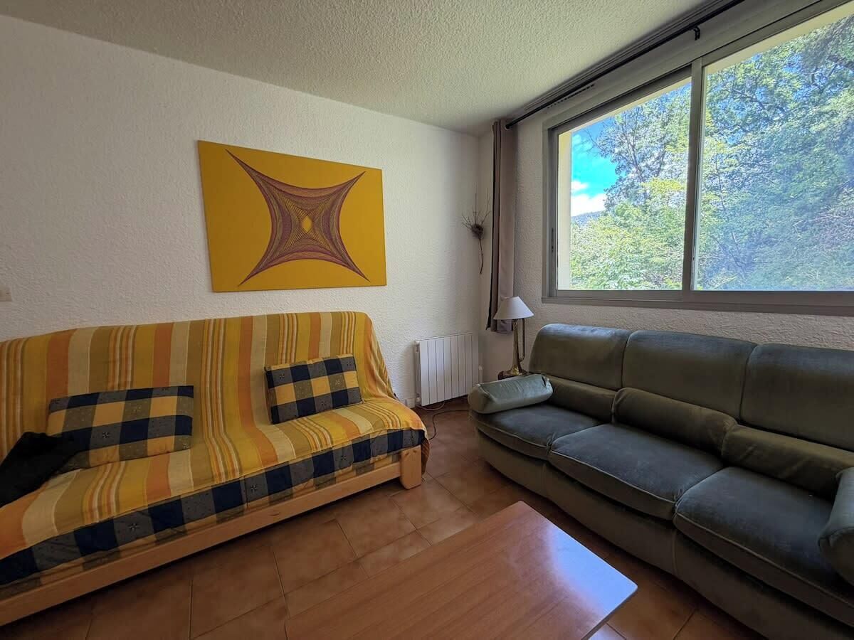 Un salon avec deux canapés, un radiateur et une fenêtre donnant sur des arbres.