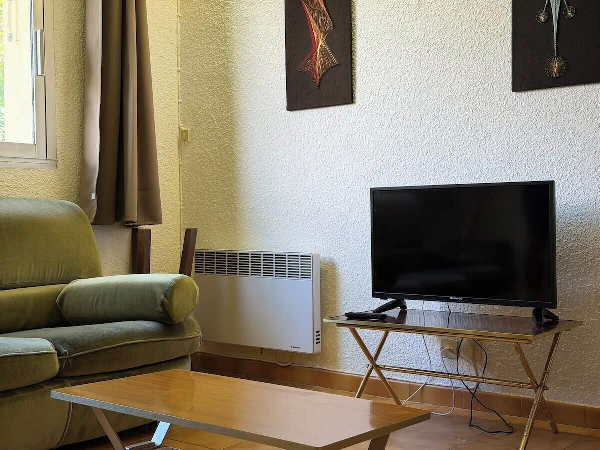 Un salon avec un canapé, un téléviseur à écran plat posé sur un meuble, un radiateur et une fenêtre avec des rideaux.