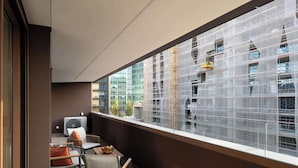 Uma varanda com vista para um prédio em construção, uma cadeira, uma mesa com frutas e um aparelho de ar condicionado.