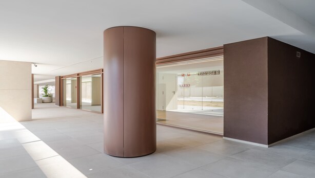 Um interior moderno com uma coluna cilíndrica grande, entrada por porta de vidro e piso revestido de azulejos.