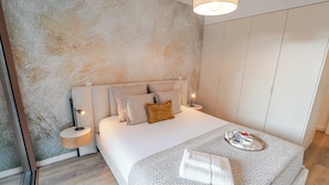 Quarto moderno com cama, mesas de cabeceira, armário e parede texturizada.