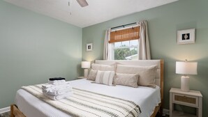 Un letto rifatto con coperta a righe, due lampade ai lati del letto, una finestra con tende e un comodino con una lampada.