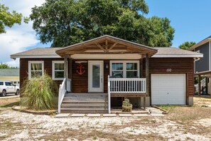 A two-story wooden house with a front porch, a garage, and a large tree in the background. - Pet-Friendly Oak Island Home W/ Fenced Yard &Fire Pit (Oak Island)