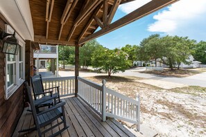 A wooden porch with a white railing, two rocking chairs, and a view of a residential area with trees and houses. - Pet-Friendly Oak Island Home W/ Fenced Yard &Fire Pit (Oak Island)