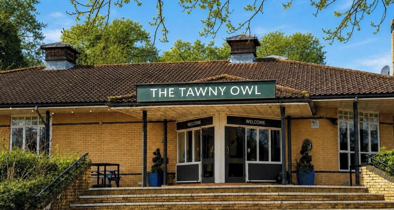 En byggnad med en skylt som visar texten ”THE TAWNY OWL” och en skylt med texten ”VÄLKOMMEN” vid ingången.