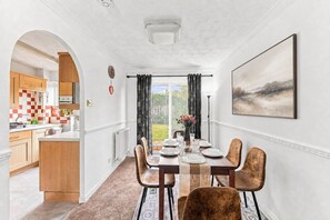 Comedor con mesa dispuesta para seis, cocina visible a través de un arco, y un cuadro grande en la pared.