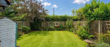A well-maintained backyard with a wooden fence, a shed, and a variety of plants.