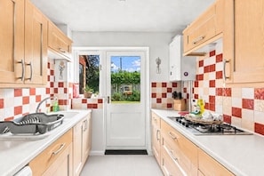 A compact kitchen with a white door leading to a garden, checkered red and white tiles, wooden cabinets, and a gas stove.