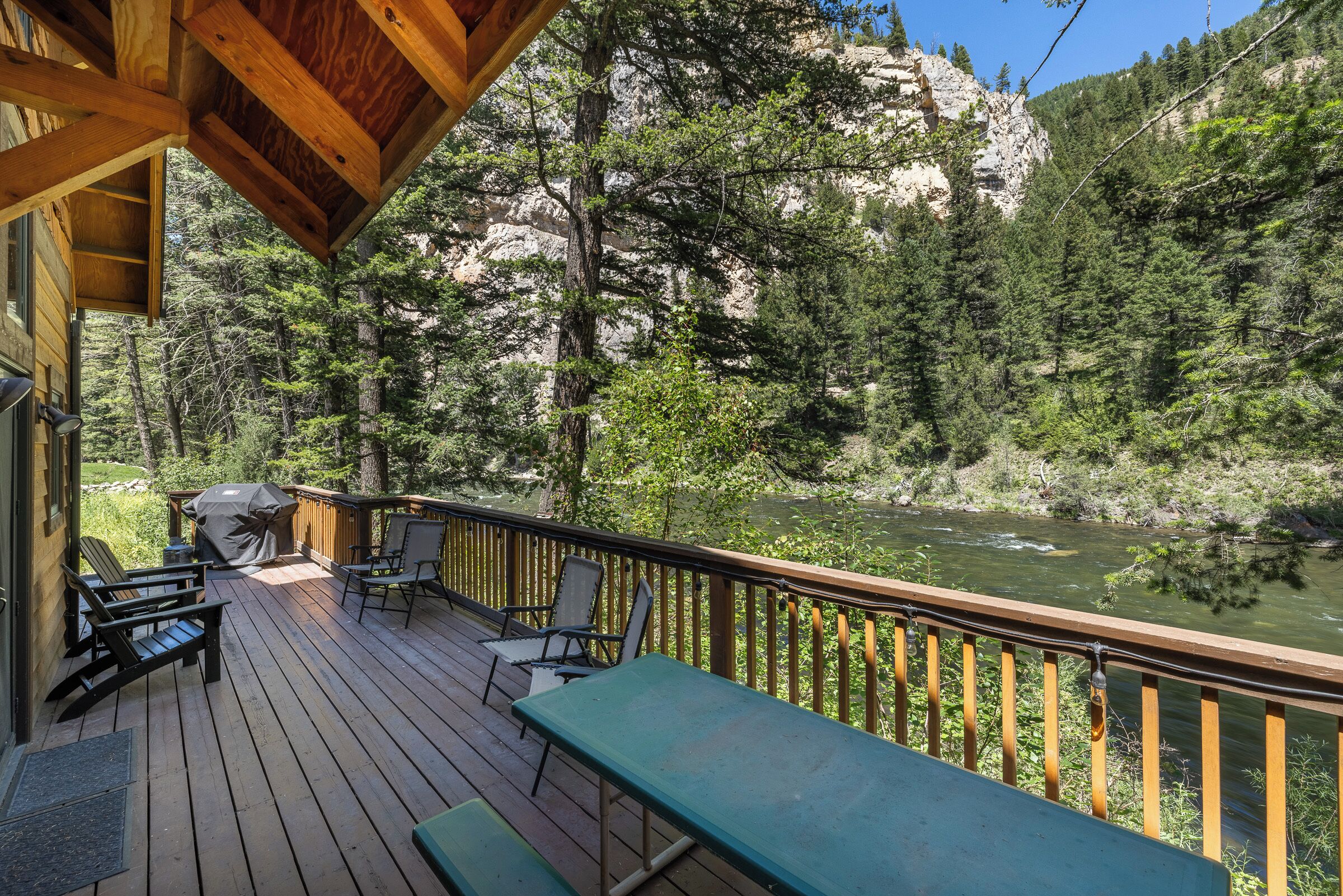 A wooden deck with outdoor furniture, overlooking a river and forested mountains.