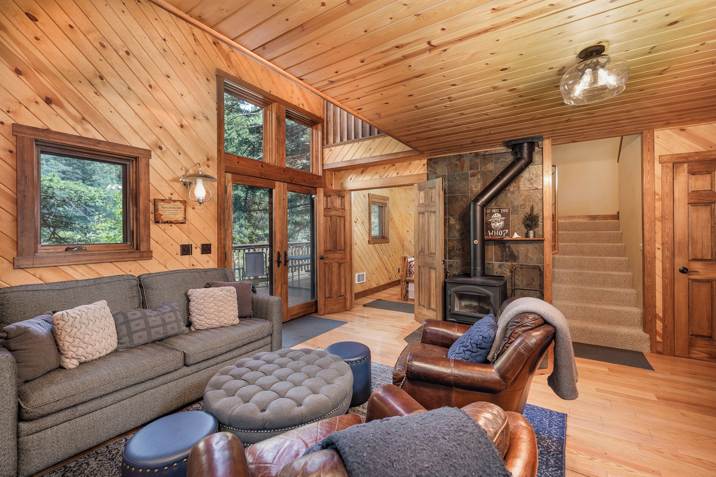 A wooden interior with a sofa, ottoman, leather chair, and a fireplace.