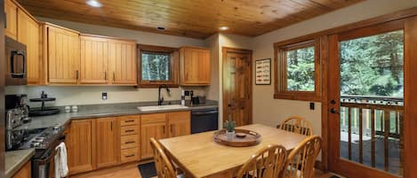 Una cocina de madera con una mesa de comedor y sillas, armarios de madera y vistas al exterior a través de ventanas amplias.