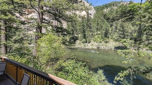 A deck overlooking a river with dense forest and rocky cliffs.