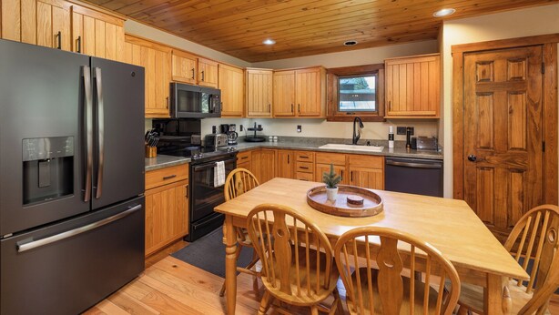 A modern kitchen with wooden cabinets, stainless steel appliances, and a dining area with a wooden table and chairs.