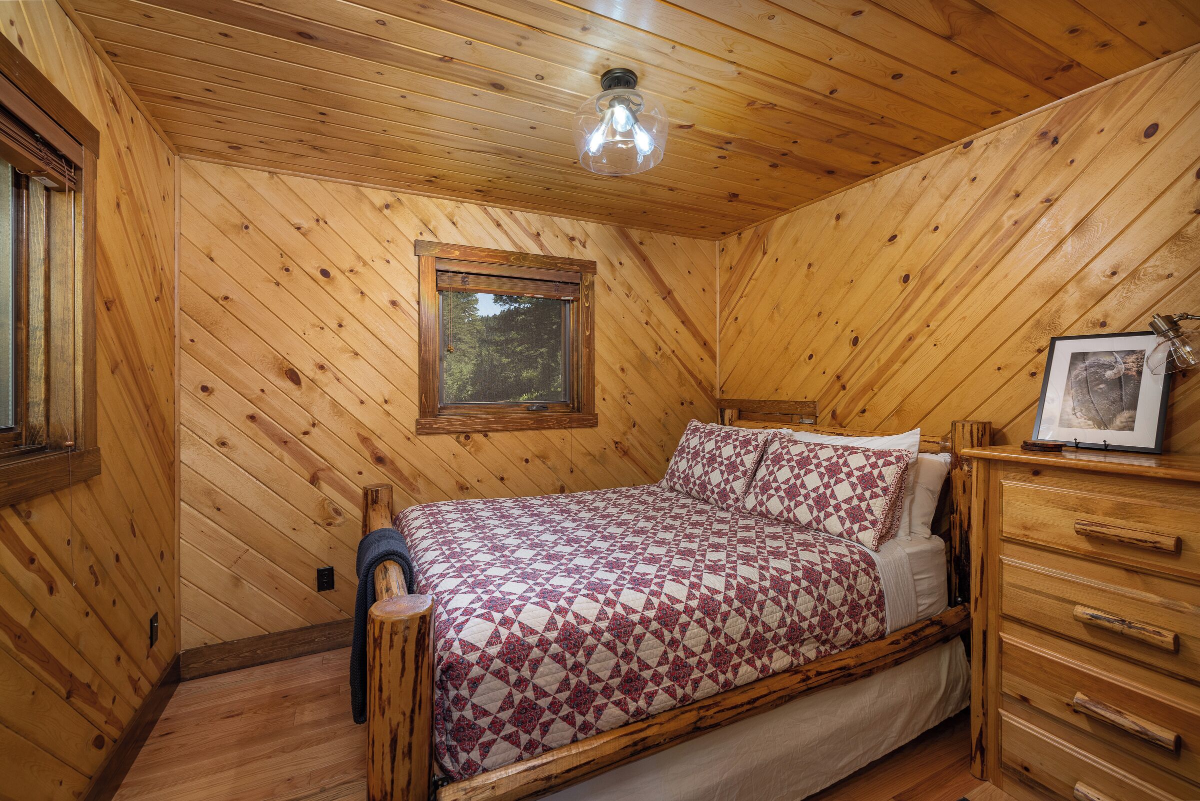 A wooden-paneled room with a bed, a dresser, and a window.