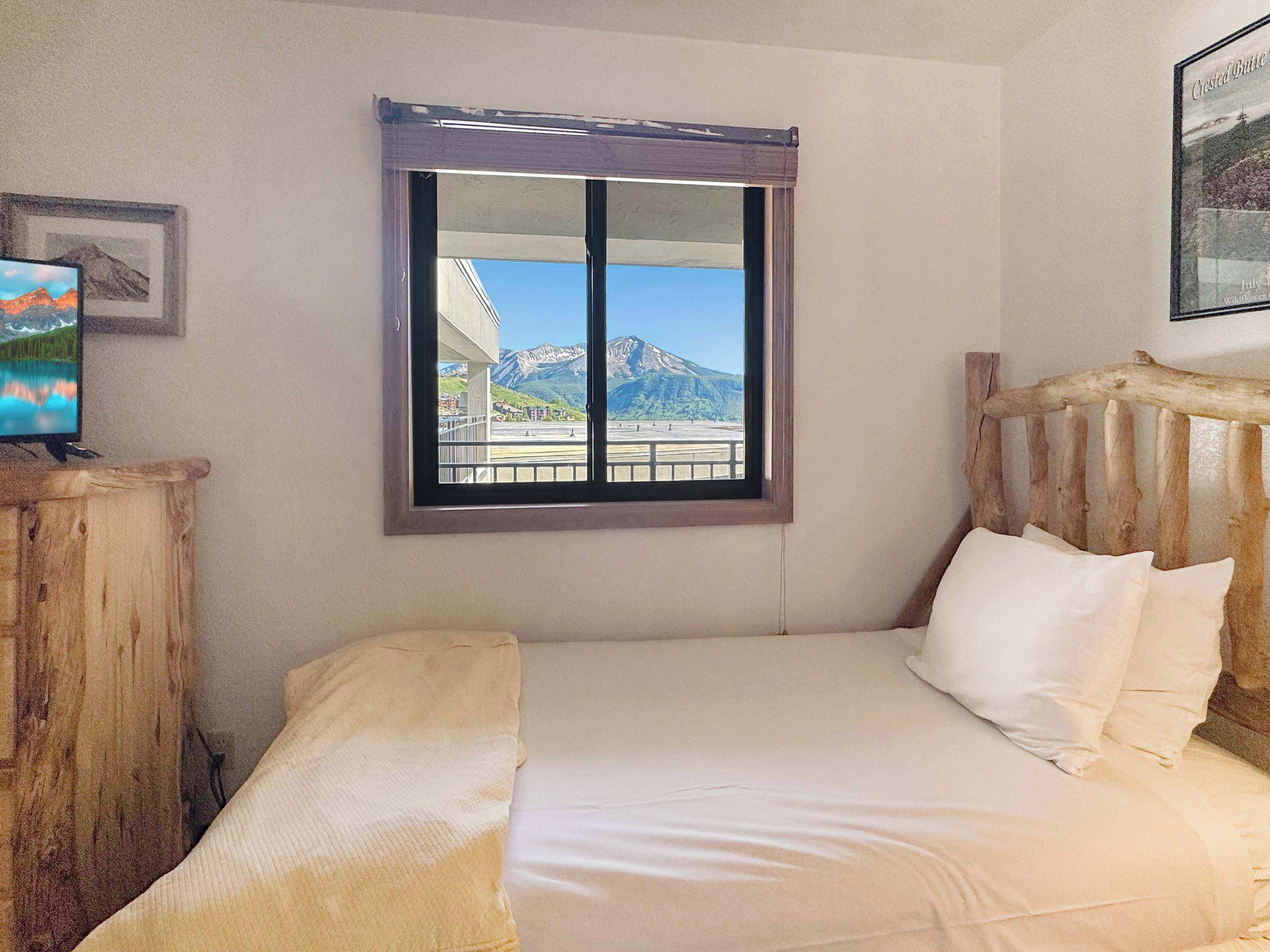 Une chambre à coucher avec un lit, une fenêtre donnant sur les montagnes, une tête de lit en bois et un téléviseur posé sur une commode en bois.