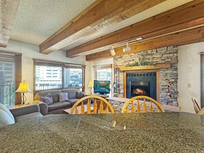A living room with a stone fireplace, a sofa, a dining table, and a television. - NEW LISTING | Plaza 641 at Woodcreek — 2BR Walk to Crested Butte Lifts (Crested Butte)