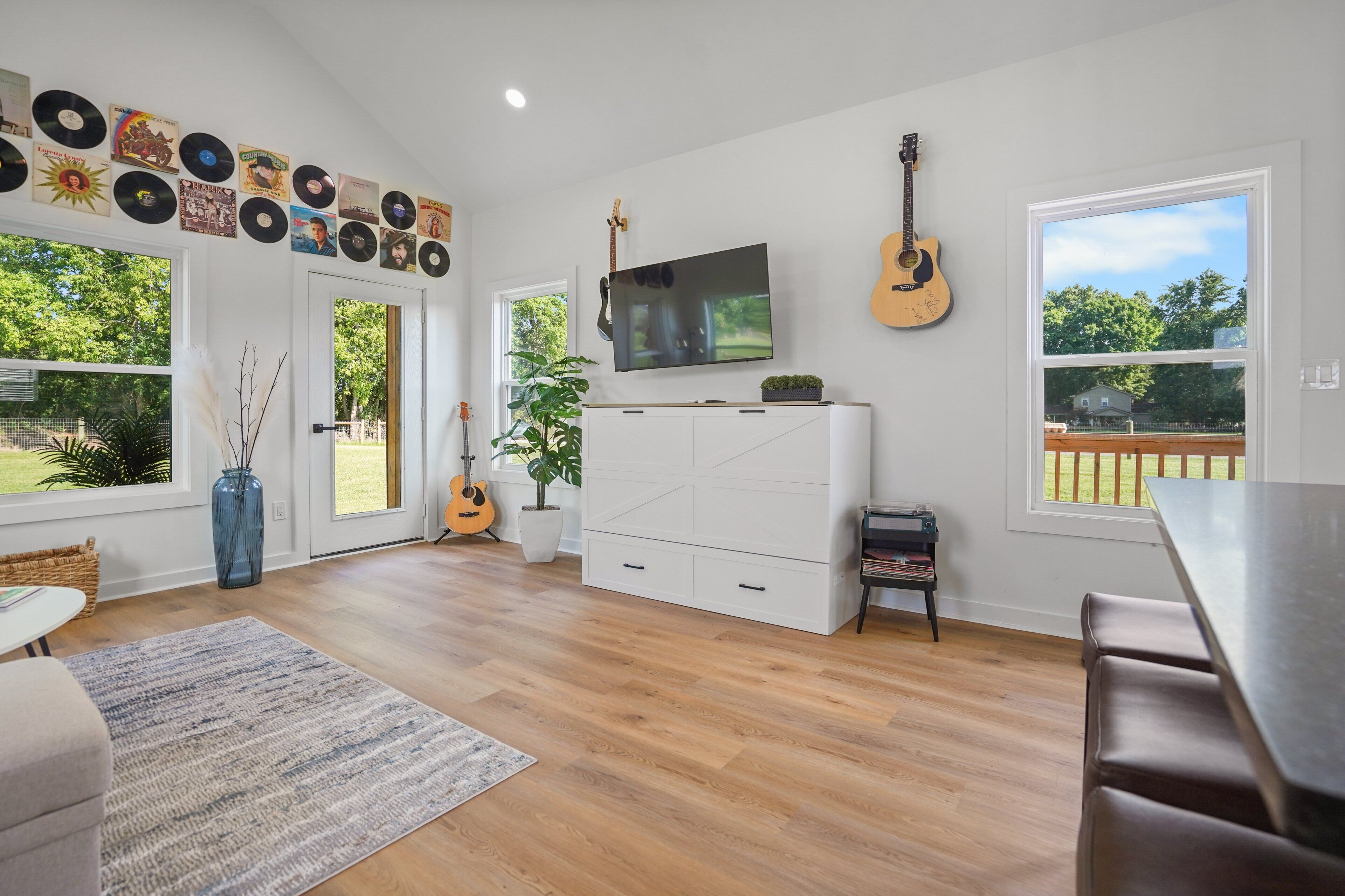 Une pièce spacieuse avec une grande fenêtre, un téléviseur à écran plat, une guitare et une collection de disques vinyle accrochés au mur.
