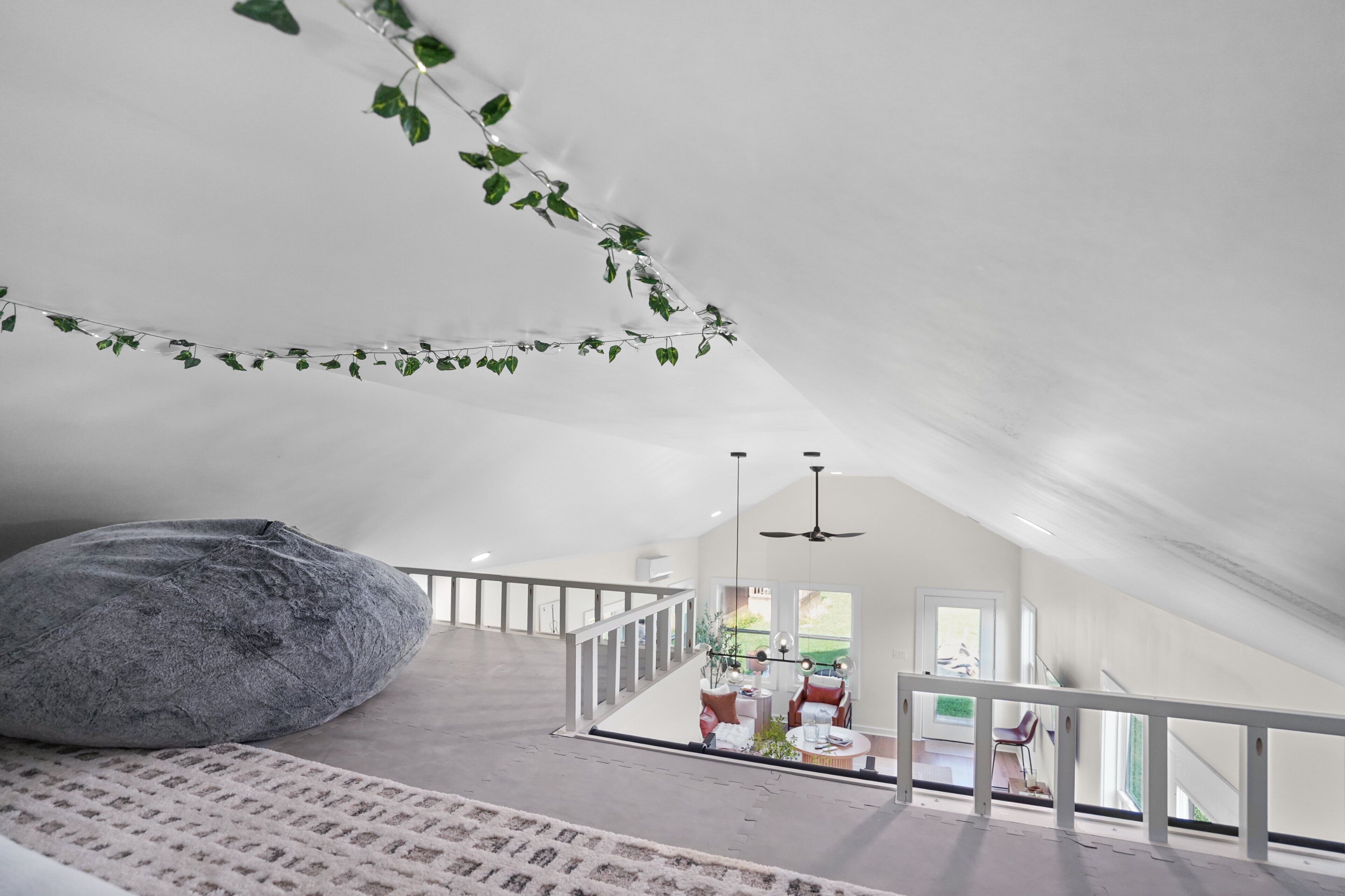 Une pièce mansardée spacieuse, avec un grand fauteuil en forme de poire, un plafond blanc et une vue sur le salon situé en contrebas.