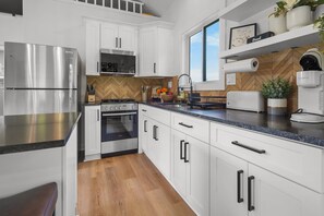Una cocina moderna con armarios blancos, electrodomésticos de acero inoxidable, un salpicadero de madera en patrón de espiga y un amplio ventanal que proporciona luz natural.