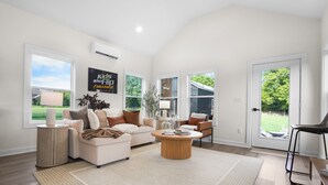 A spacious living room with a large window, a sofa set, a coffee table, and a decorative wall piece. - Hidden Gem Farm-Two Tiny Homes-Sleeps 11 (Spring Hill)