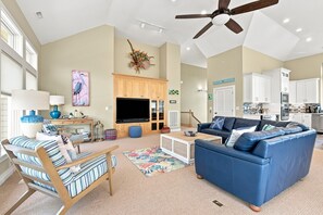 Ein geräumiges Wohnzimmer mit einem blauen Sofa, Holzmöbeln, einem Flachbildfernseher und einem Deckenventilator.