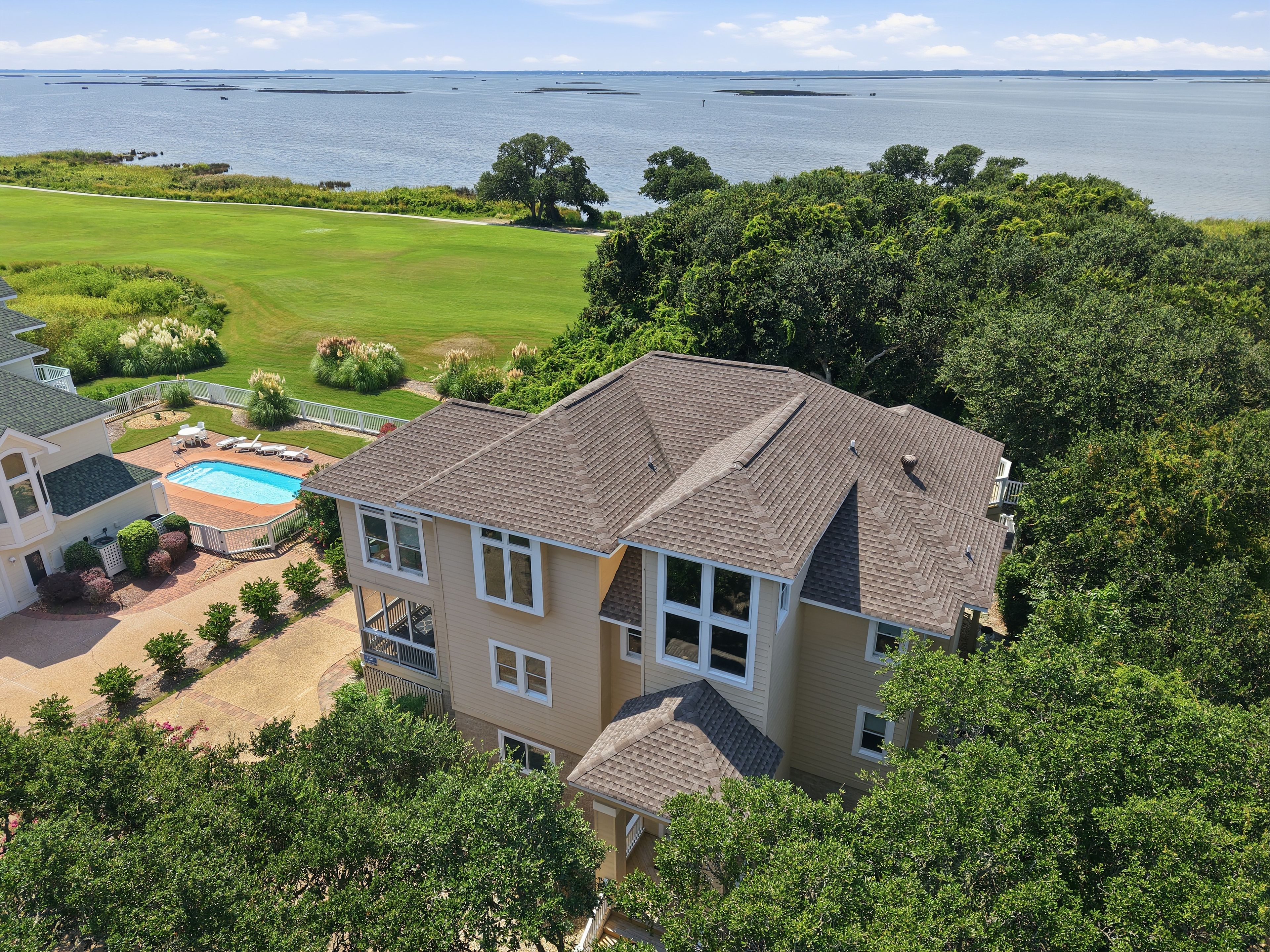 A two-story house with a swimming pool, surrounded by lush greenery and a view of the water.