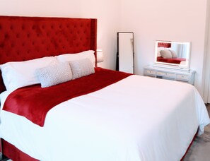 Un lit avec une tête de lit rouge, une literie blanche et un miroir posé sur une table de chevet.