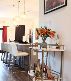 A modern kitchen with a bar area, white bar stools, a vase with flowers, and a bottle of wine. - New Gated Home Near the Texas Medical Center: Workspace + Yard +Fast Wifi (Houston)