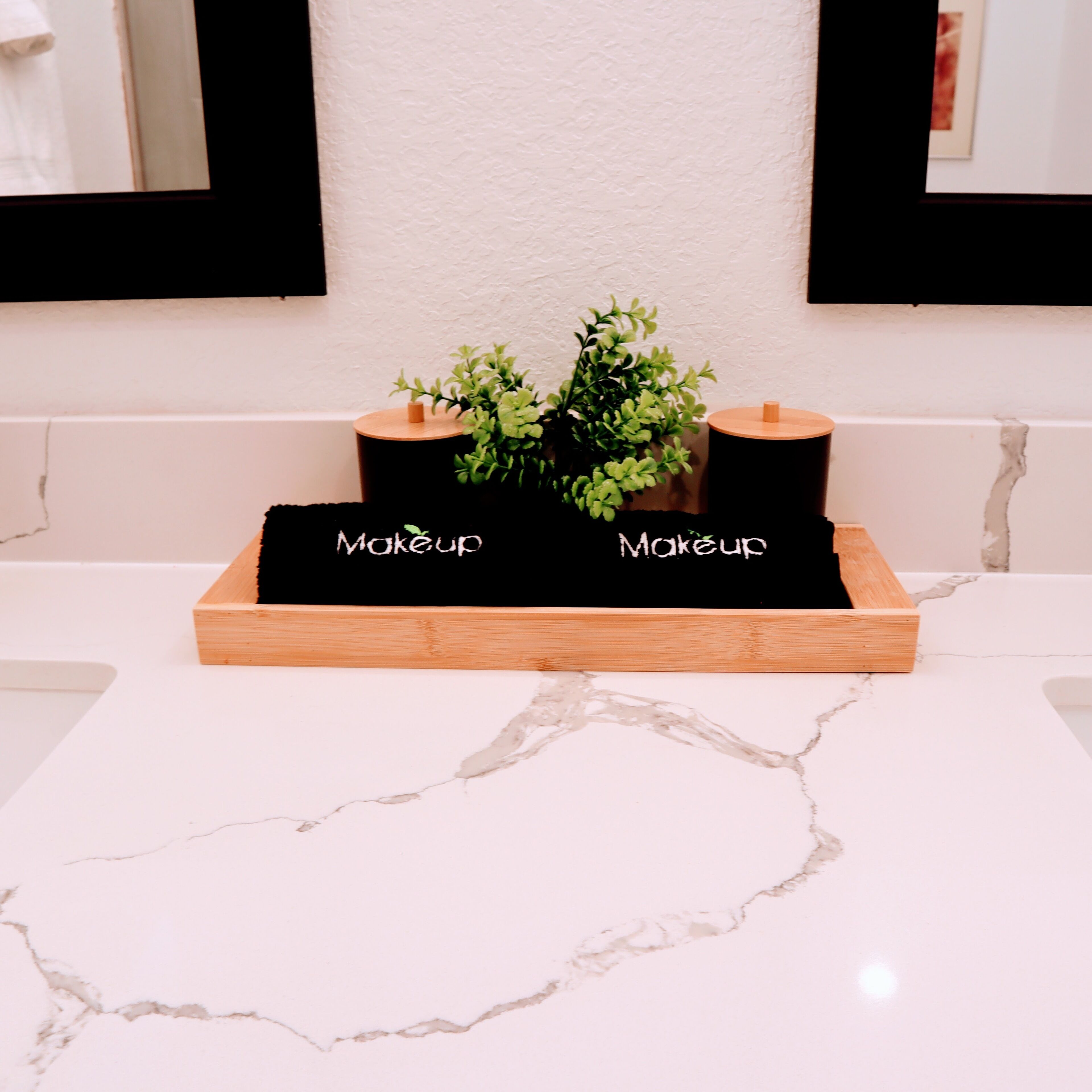A bathroom vanity with a marble countertop, two black makeup containers, and a potted plant.