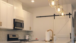 A modern kitchen with white cabinetry, a stainless steel microwave, a gas stove, and a central island with a gold faucet. - New Gated Home Near the Texas Medical Center: Workspace + Yard +Fast Wifi (Houston)