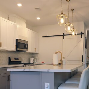A modern kitchen with white cabinetry, a stainless steel microwave, a gas stove, and a central island with a gold faucet. - New Gated Home Near the Texas Medical Center: Workspace + Yard +Fast Wifi (Houston)