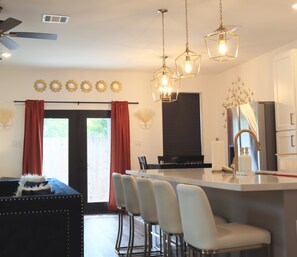 A modern kitchen with a central island, bar stools, pendant lighting, and a dining area with a view. - New Gated Home Near the Texas Medical Center: Workspace + Yard +Fast Wifi (Houston)