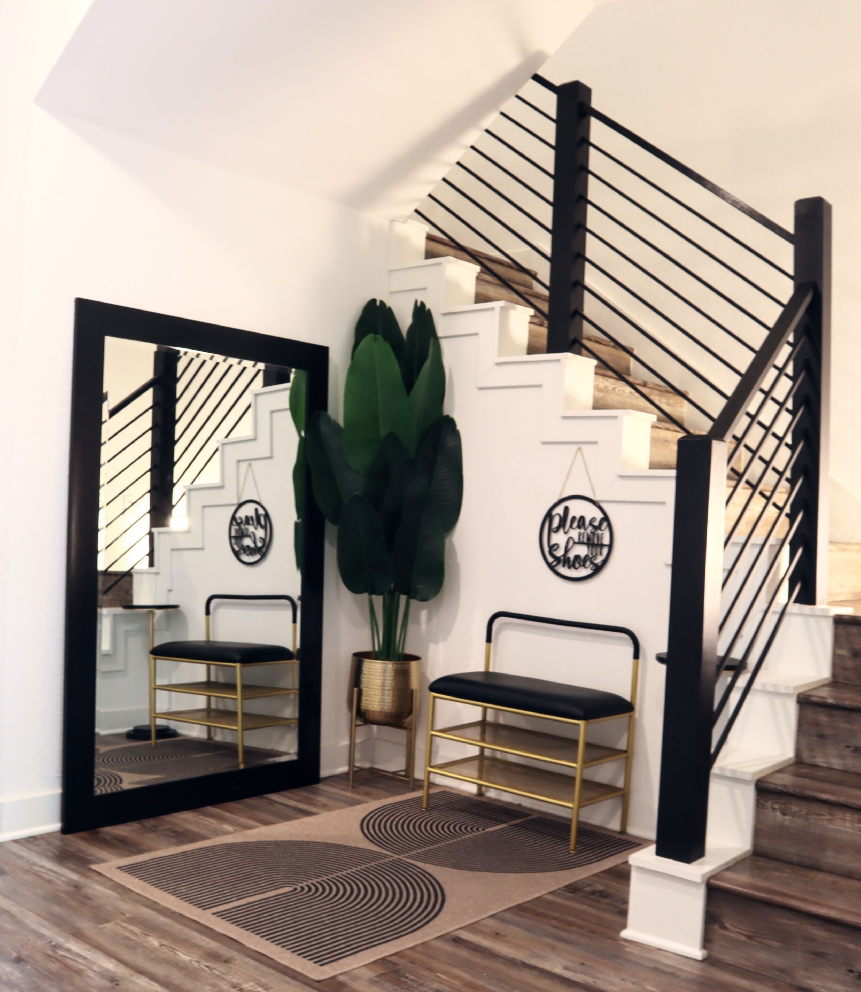 A staircase with a black handrail and a white wall with a large mirror reflecting the stairs.