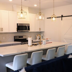 A modern kitchen with white cabinetry, a central island with bar seating, and pendant lighting. - New Gated Home Near the Texas Medical Center: Workspace + Yard +Fast Wifi (Houston)